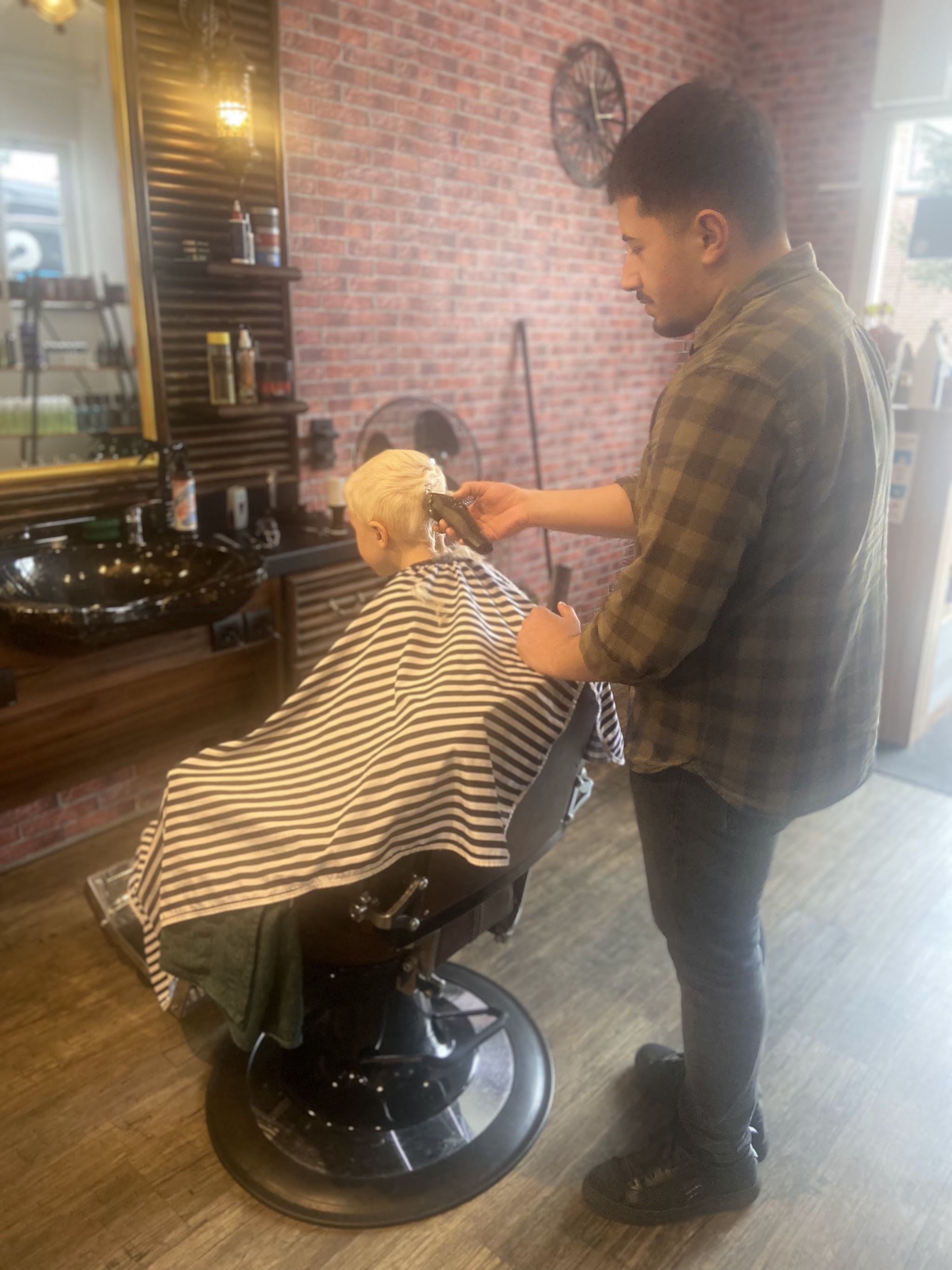 De barbier knipt een jonge klant in de kappersstoel, met spiegels en de bakstenen muur erachter